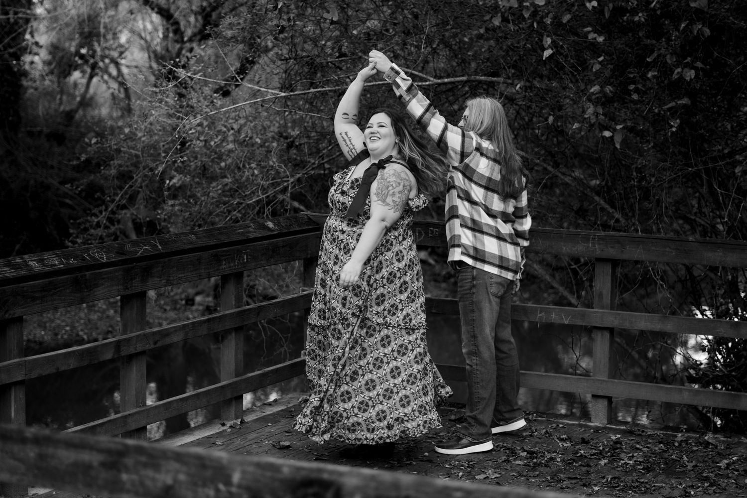 A person in a floral dress walks along a wooden boardwalk through a lush forest setting.