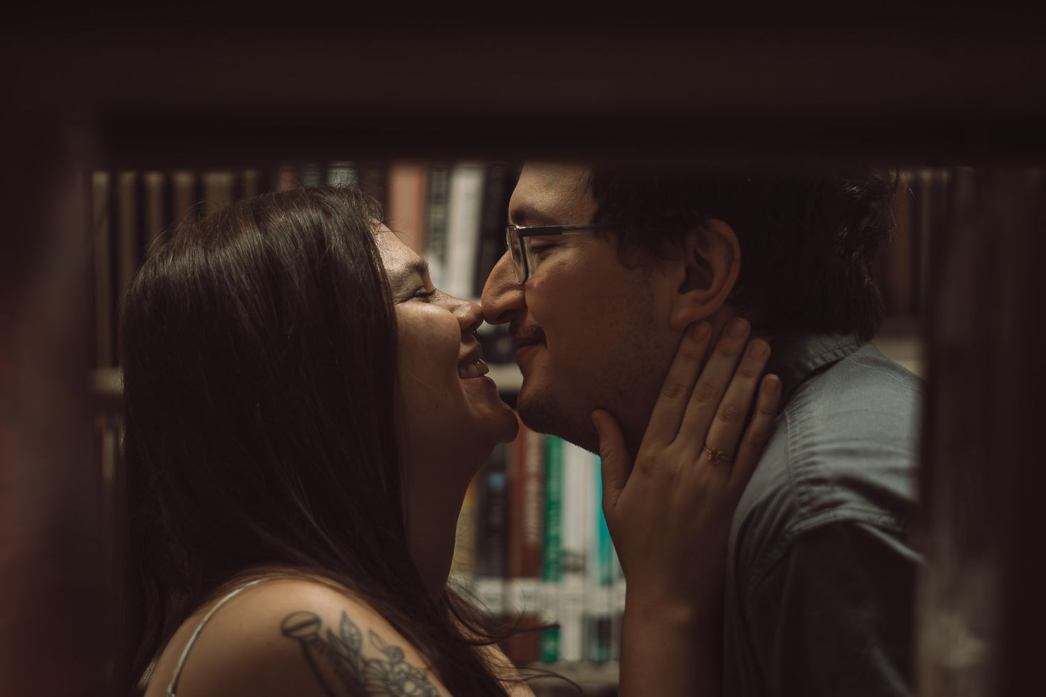 An intimate couple's photoshoot in a dimly lit library setting.