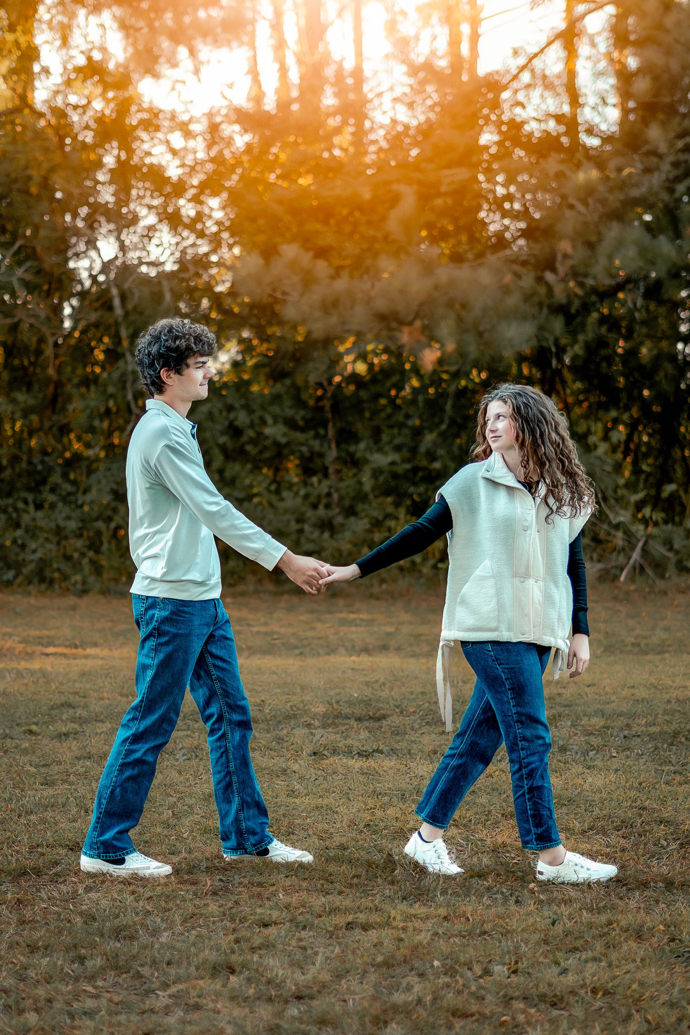 A couple in matching outfits dances and spins together in a field at sunset.