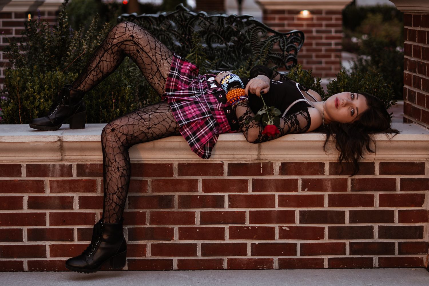 Creative fashion photo of model in plaid and lace lounging on brick wall.
