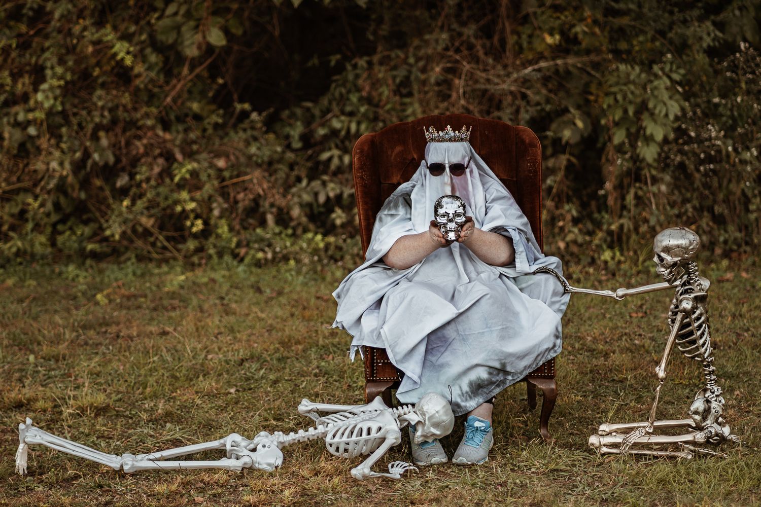 Plastic skeletons and white sheets create a ghostly Halloween display on grass.