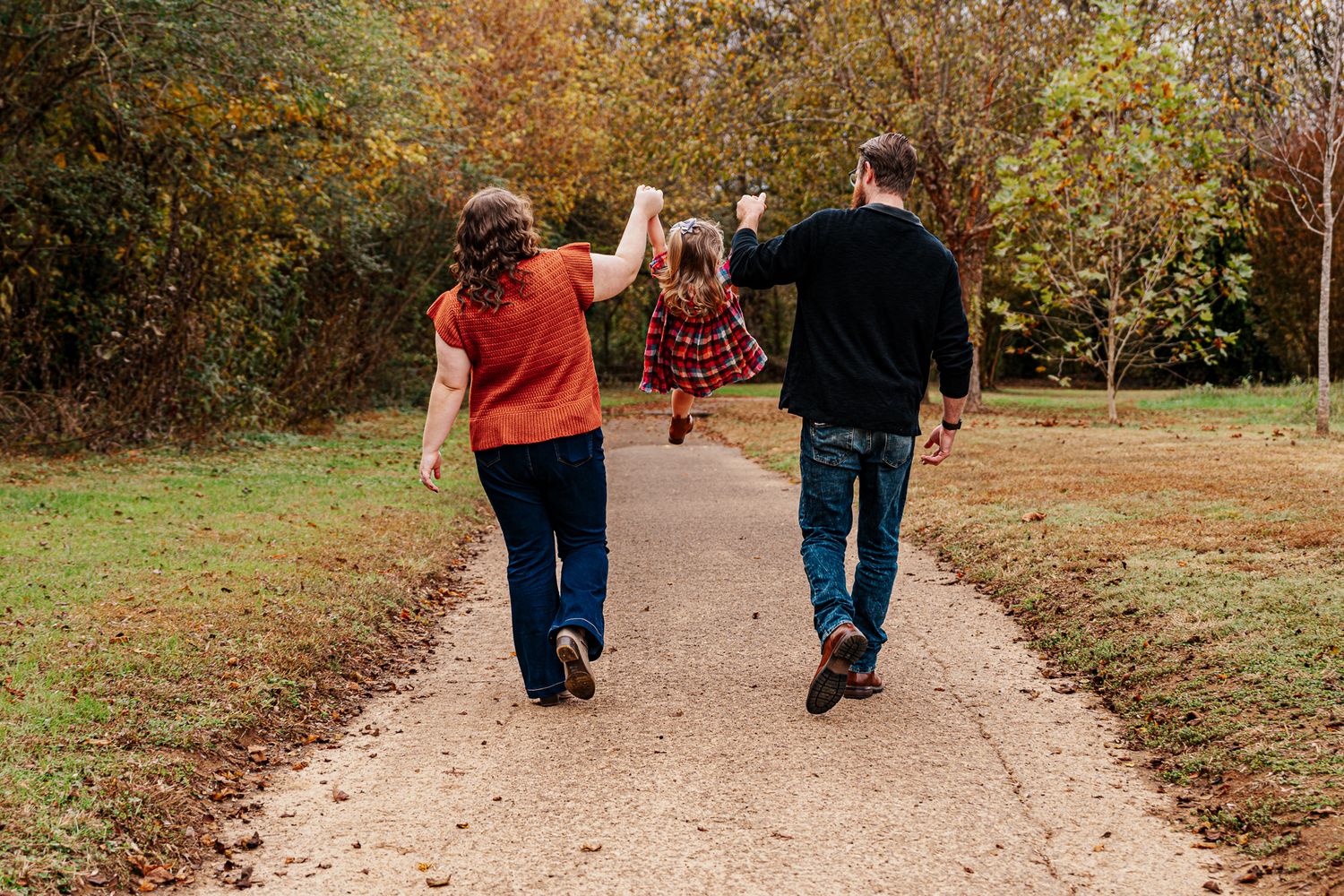 Family walking hand in hand down a tree-lined autumn path.
