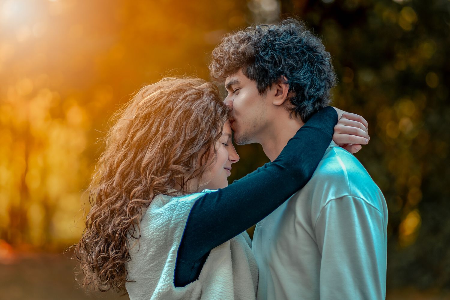 A romantic couple shares a tender moment at sunset in an outdoor setting with warm golden lighting.