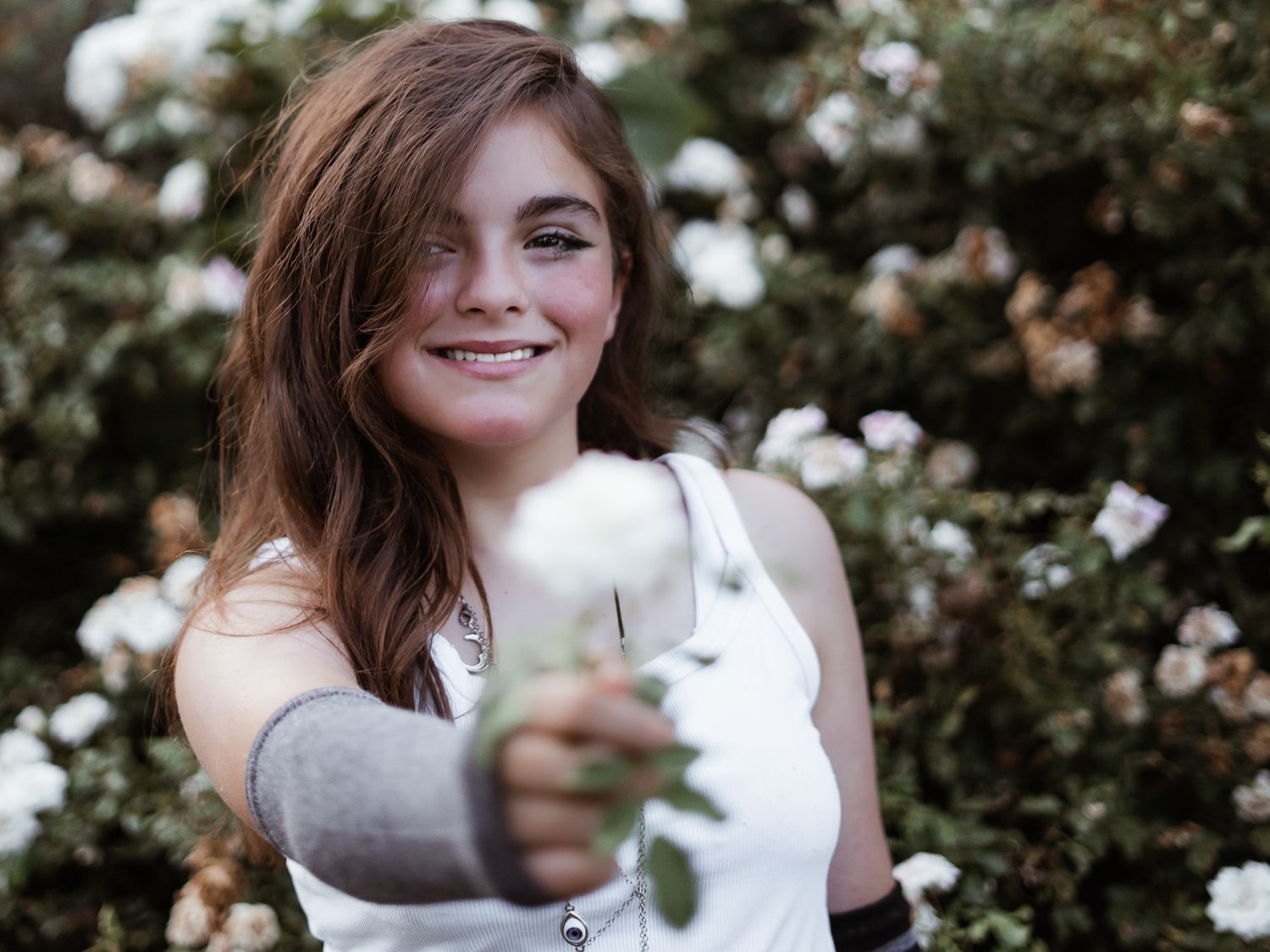 A person in white holds delicate white flowers against a natural outdoor background.