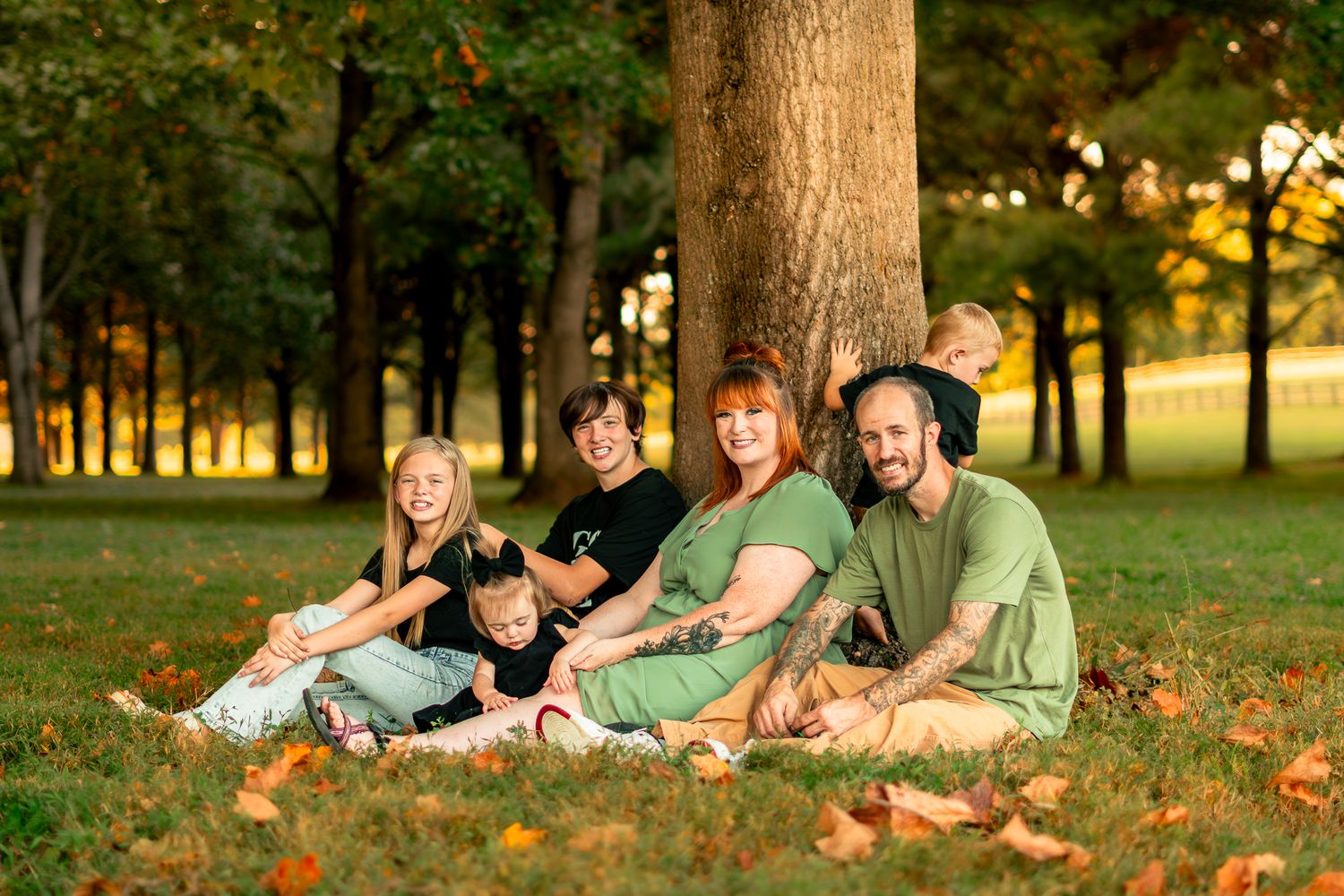 Family lying on grass together under trees during autumn sunset.