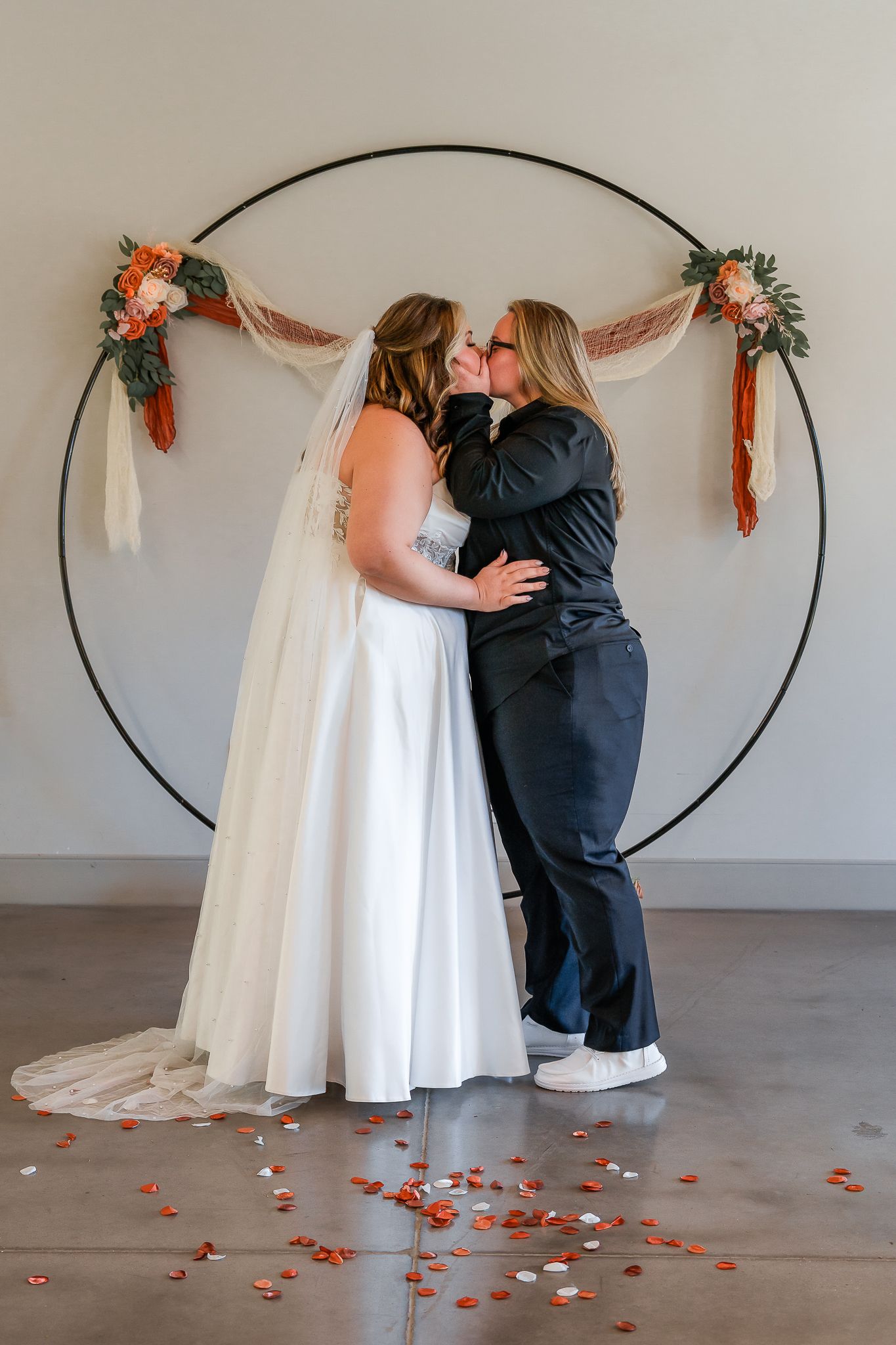 First look wedding moment captured against white backdrop with floral arch and rose petals.