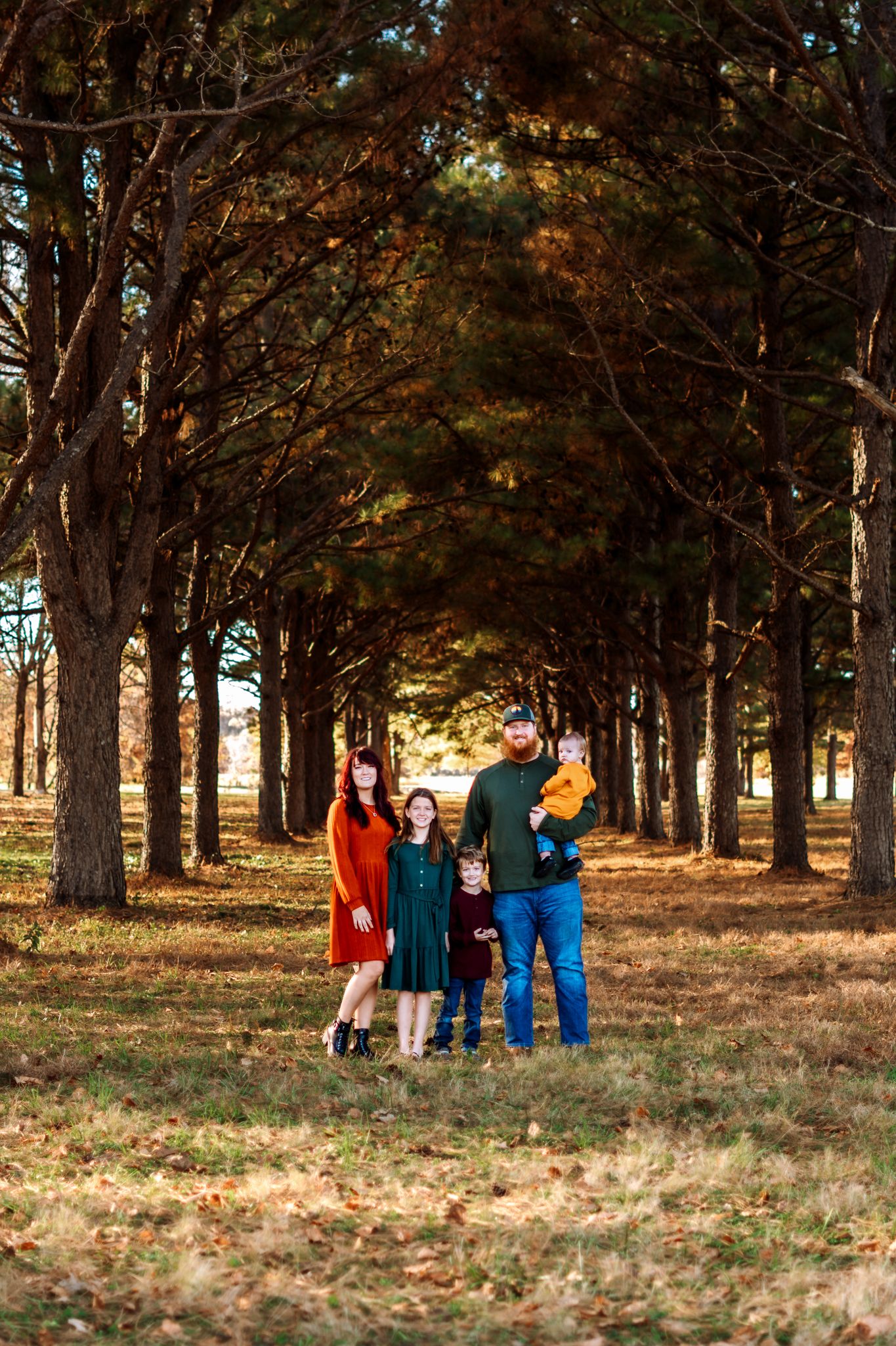 A group of people walk together through a wooded area with autumn trees and fallen leaves on the ground.