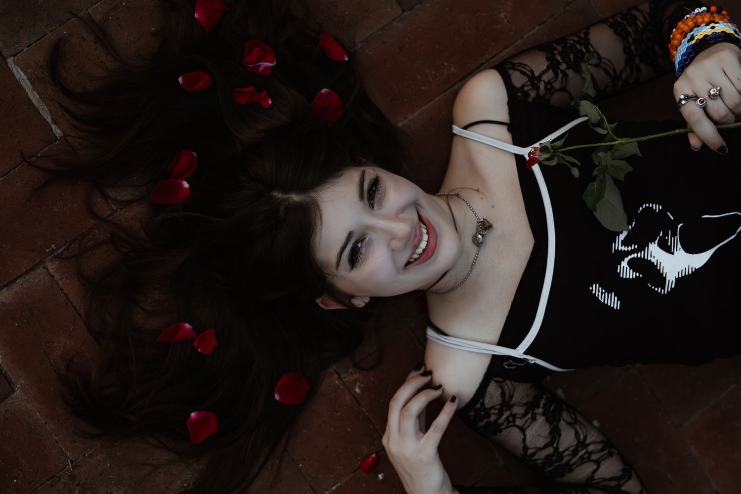 Overhead portrait with scattered red rose petals on dark surface.