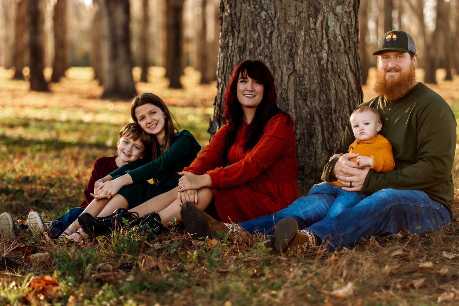 Family relaxes together on autumn ground with fallen leaves in warm evening sunlight.