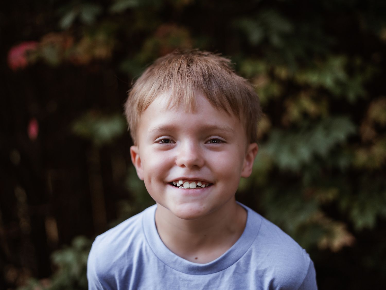 A young child smiles brightly at the camera while outdoors.