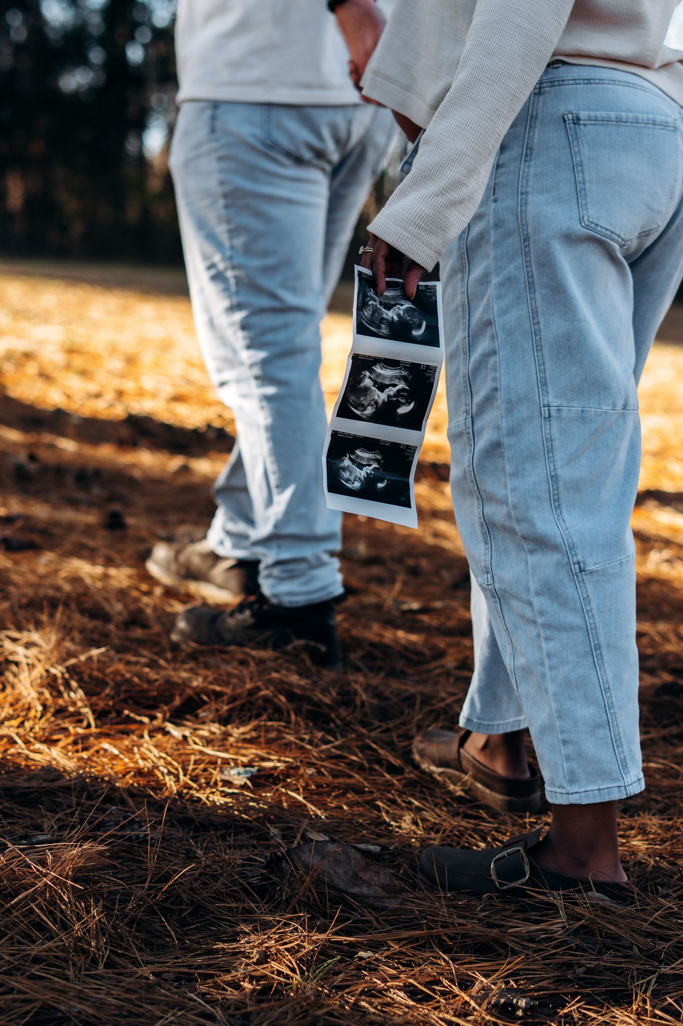 Close-up of denim pockets with ultrasound photos showing a pregnancy announcement in natural outdoor lighting.
