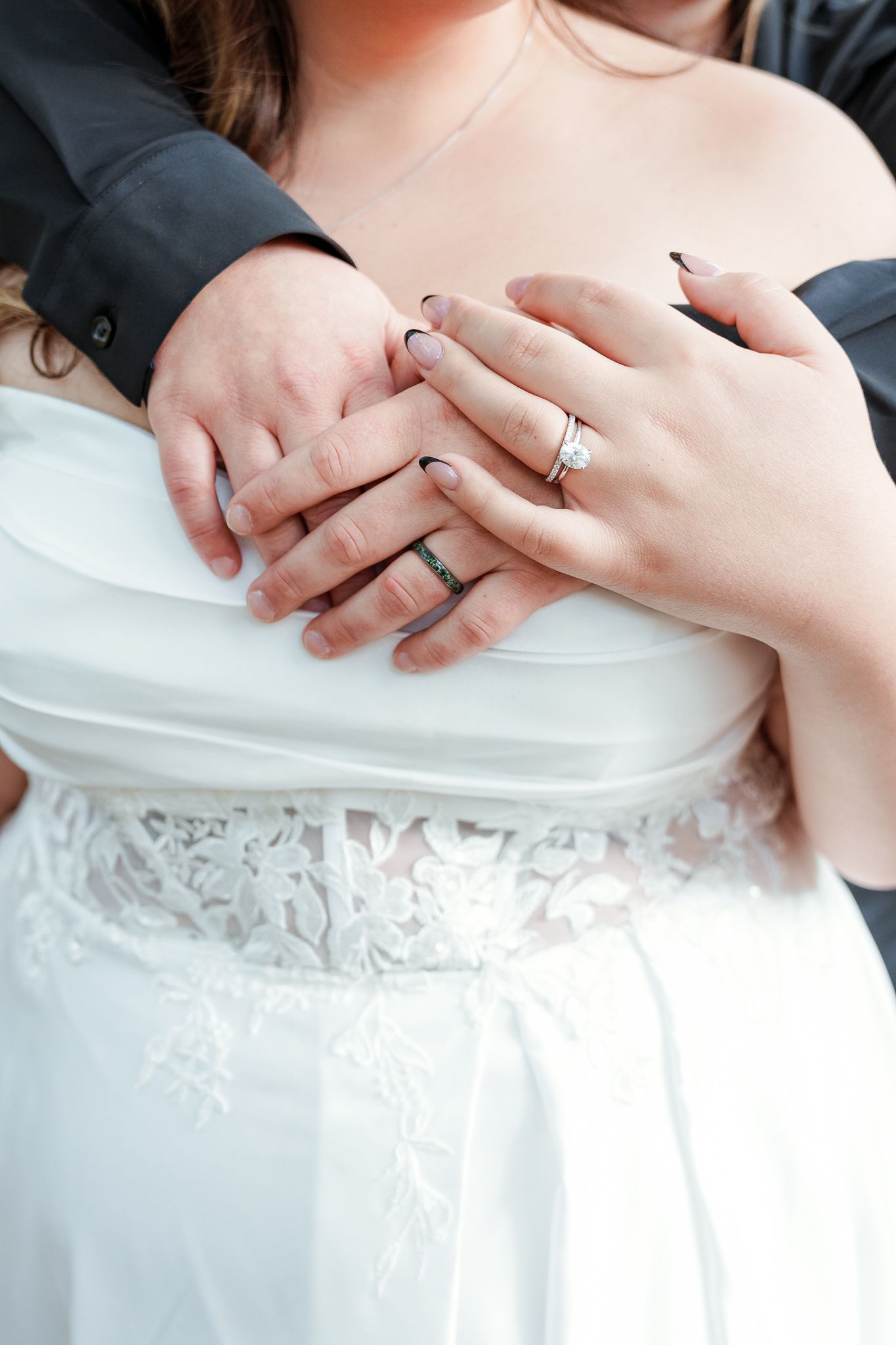 Close-up of hands exchanging rings against a white lace dress background.