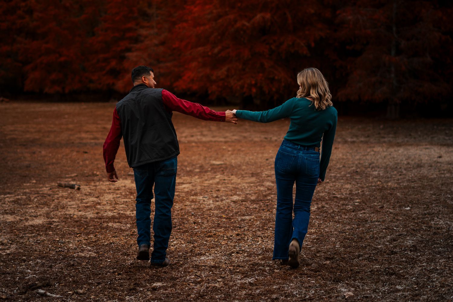 Two people walking together on a rustic autumn path through fallen leaves and reddish scenery.