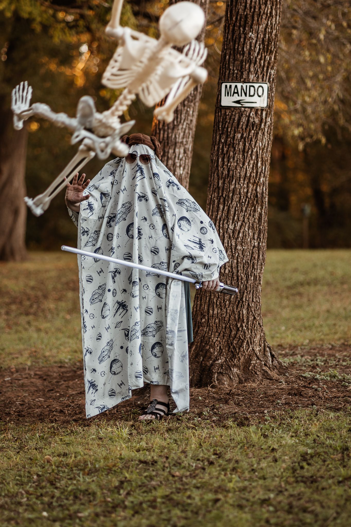 Skeletons and ghost figures arranged in a playful Halloween scene under autumn trees.