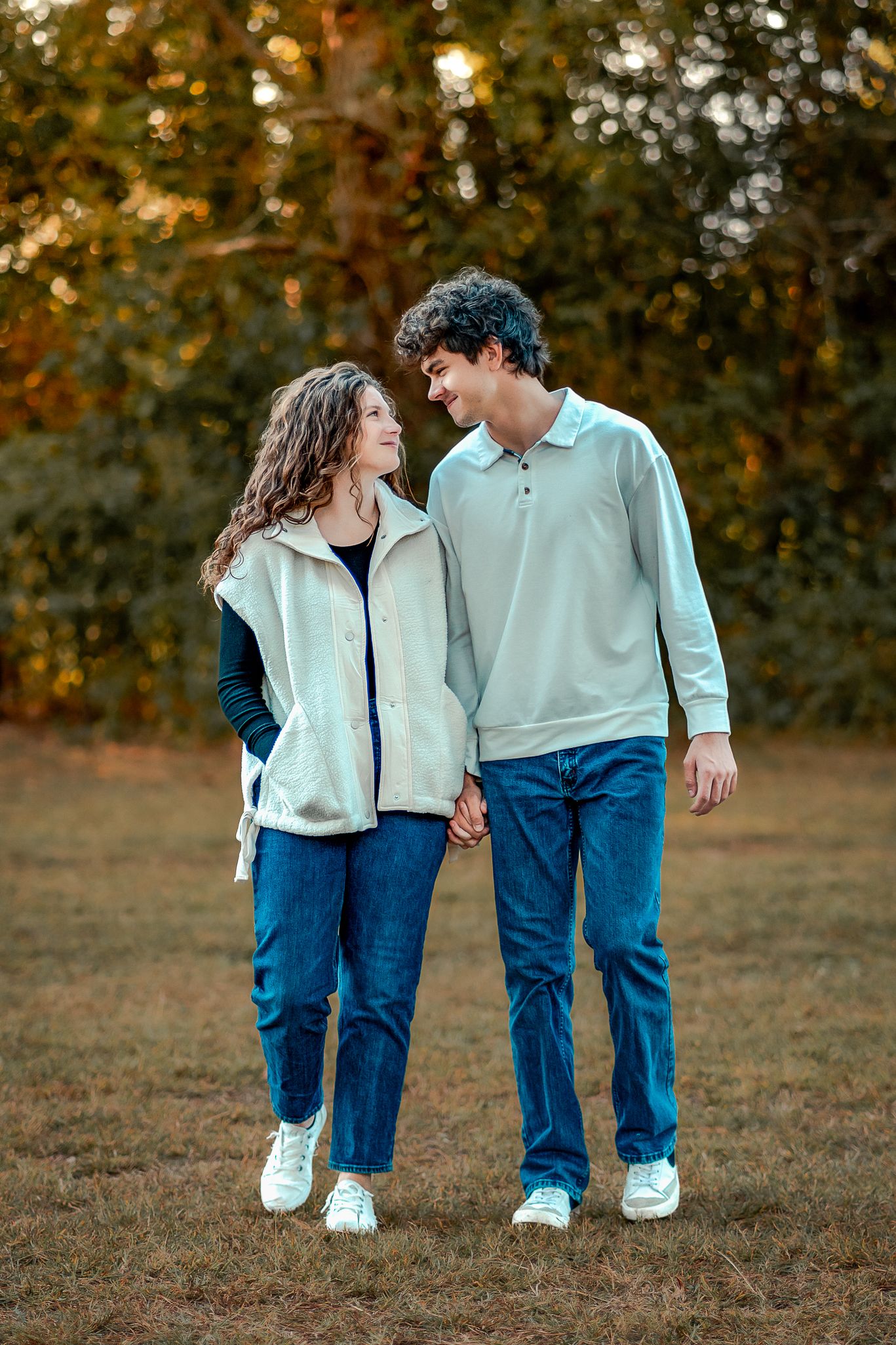 A couple in matching white tops and blue jeans share romantic moments in a fall outdoor setting.
