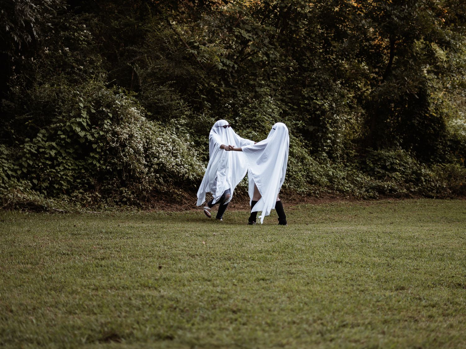 White ghostly figures drift across a grassy lawn in an outdoor Halloween display.