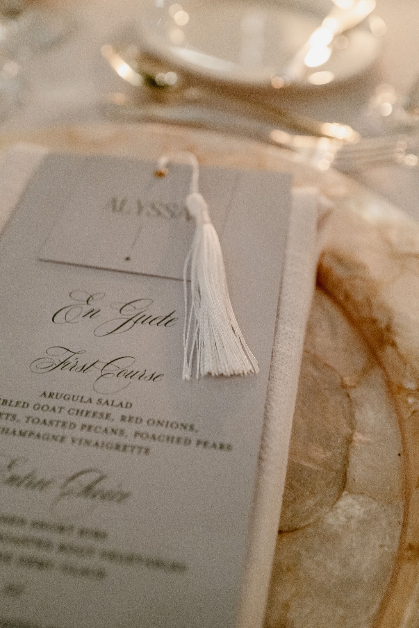 Wedding menu cards with white tassels and elegant calligraphy displaying dinner course details.