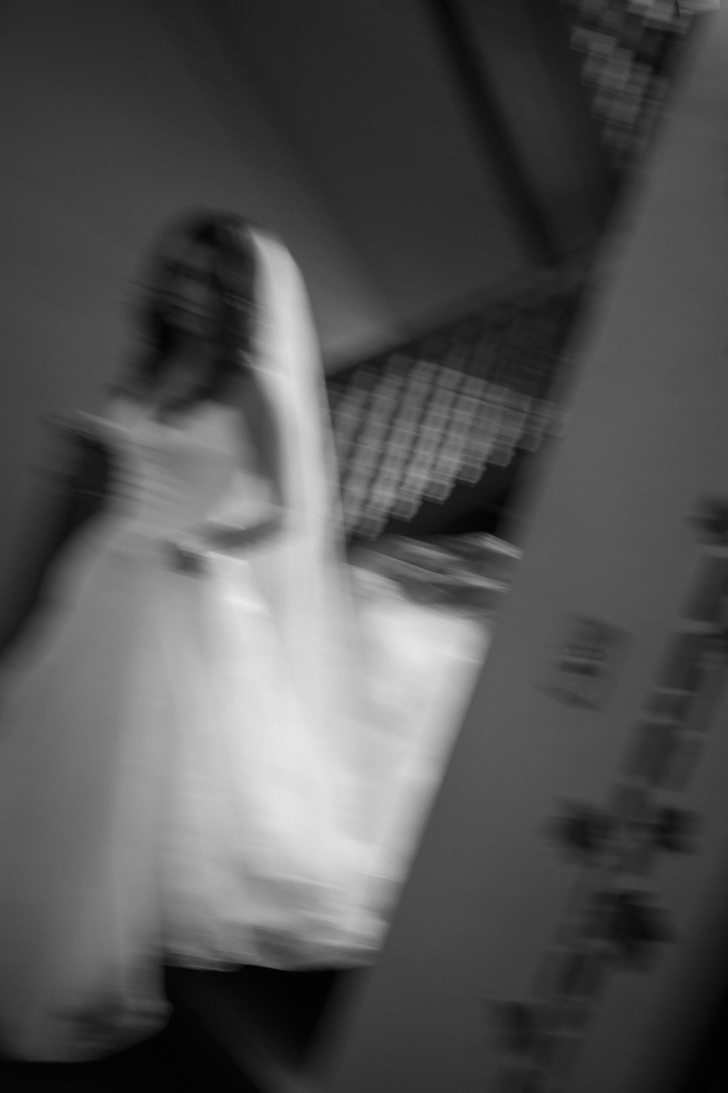 Blurry black and white photo of a woman in a white wedding dress near a staircase.
