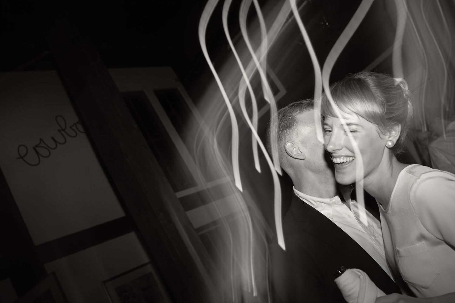 Black and white photo of a joyful couple sharing a romantic moment with light streaks creating an artistic effect.
