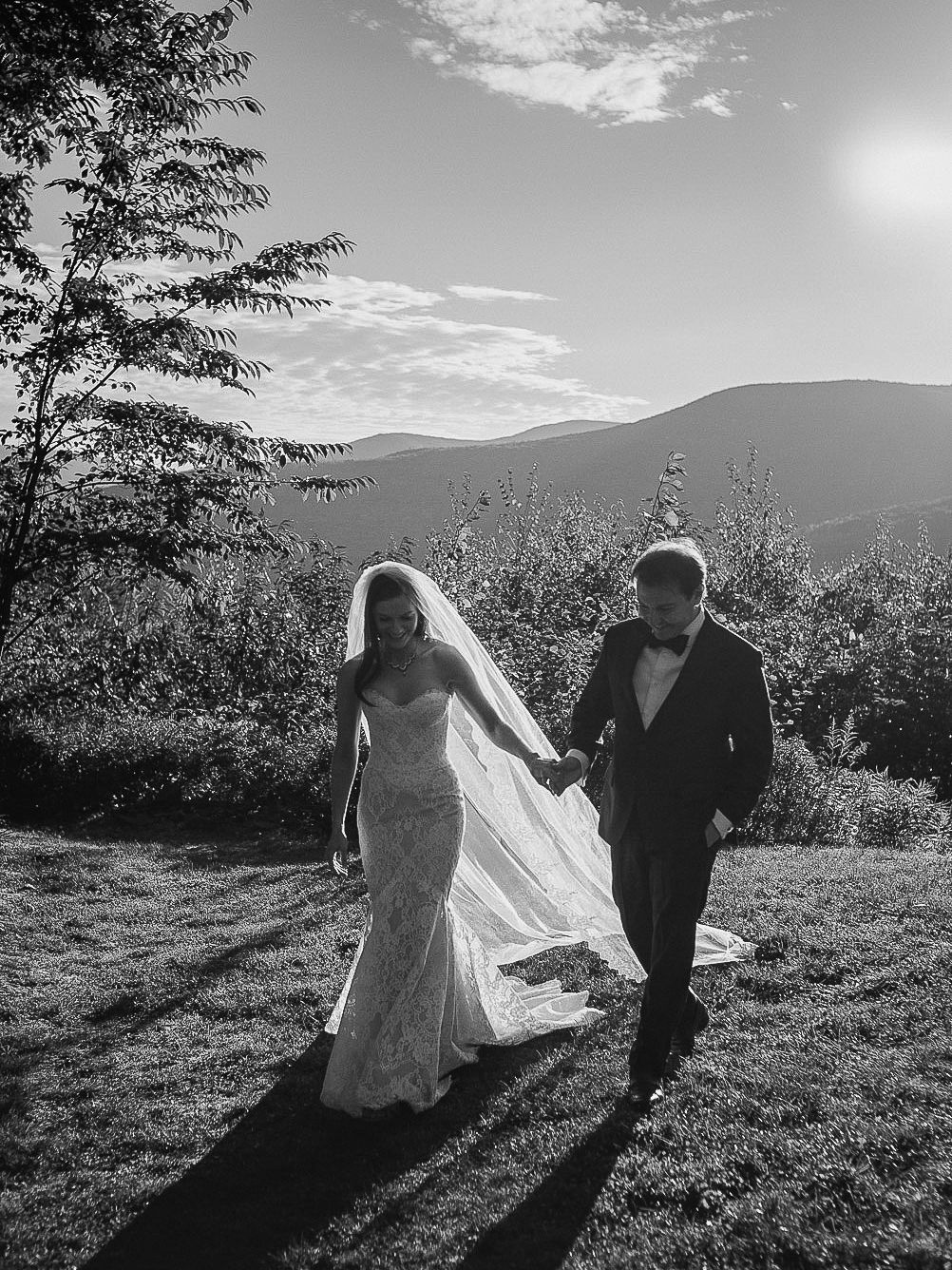 A couple in wedding attire stands in silhouette against a scenic mountain backdrop during a sunset photoshoot.