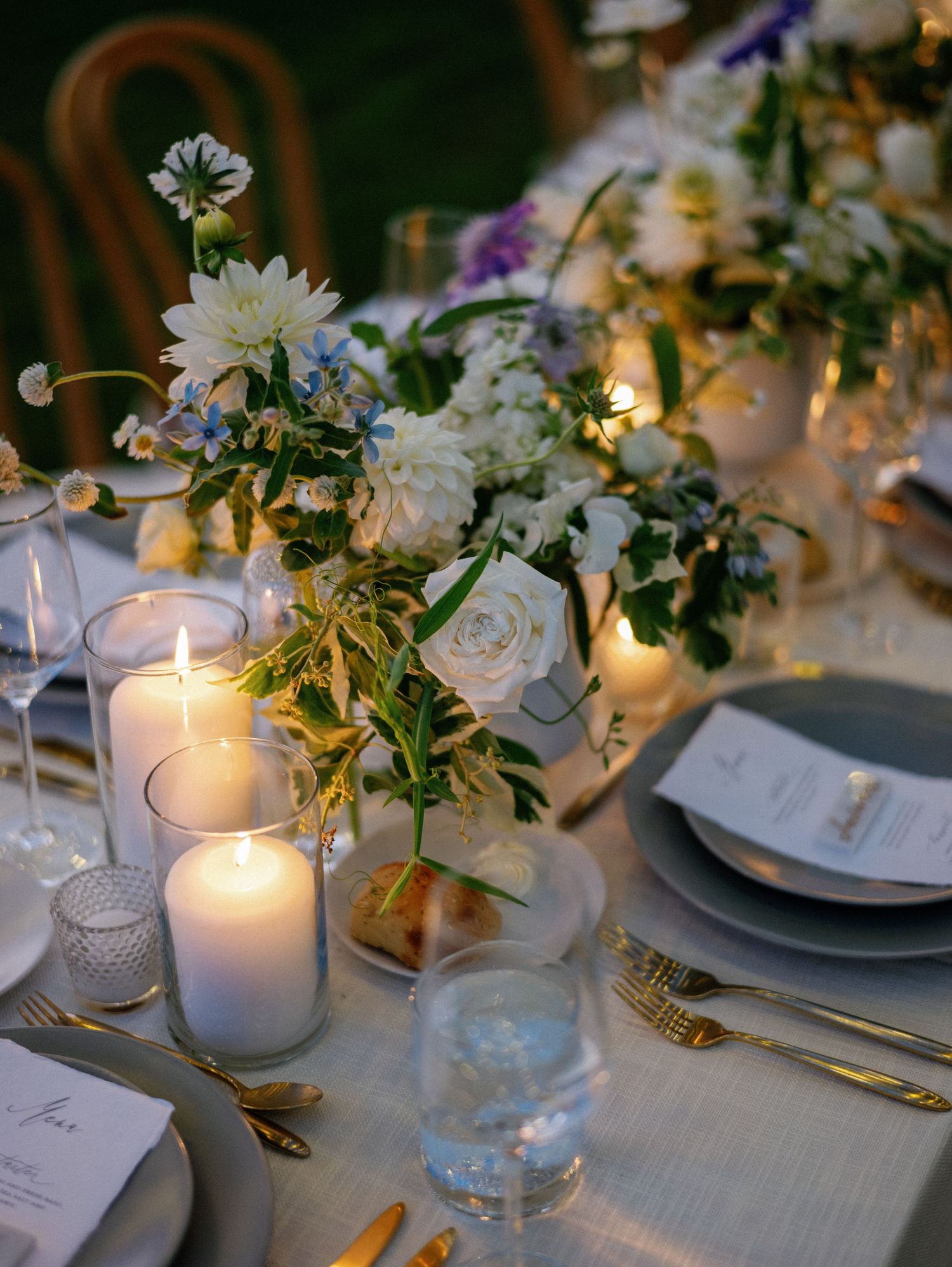 Elegant wedding reception table setting with white flowers, glowing candles, and gold accents on crisp white linens.