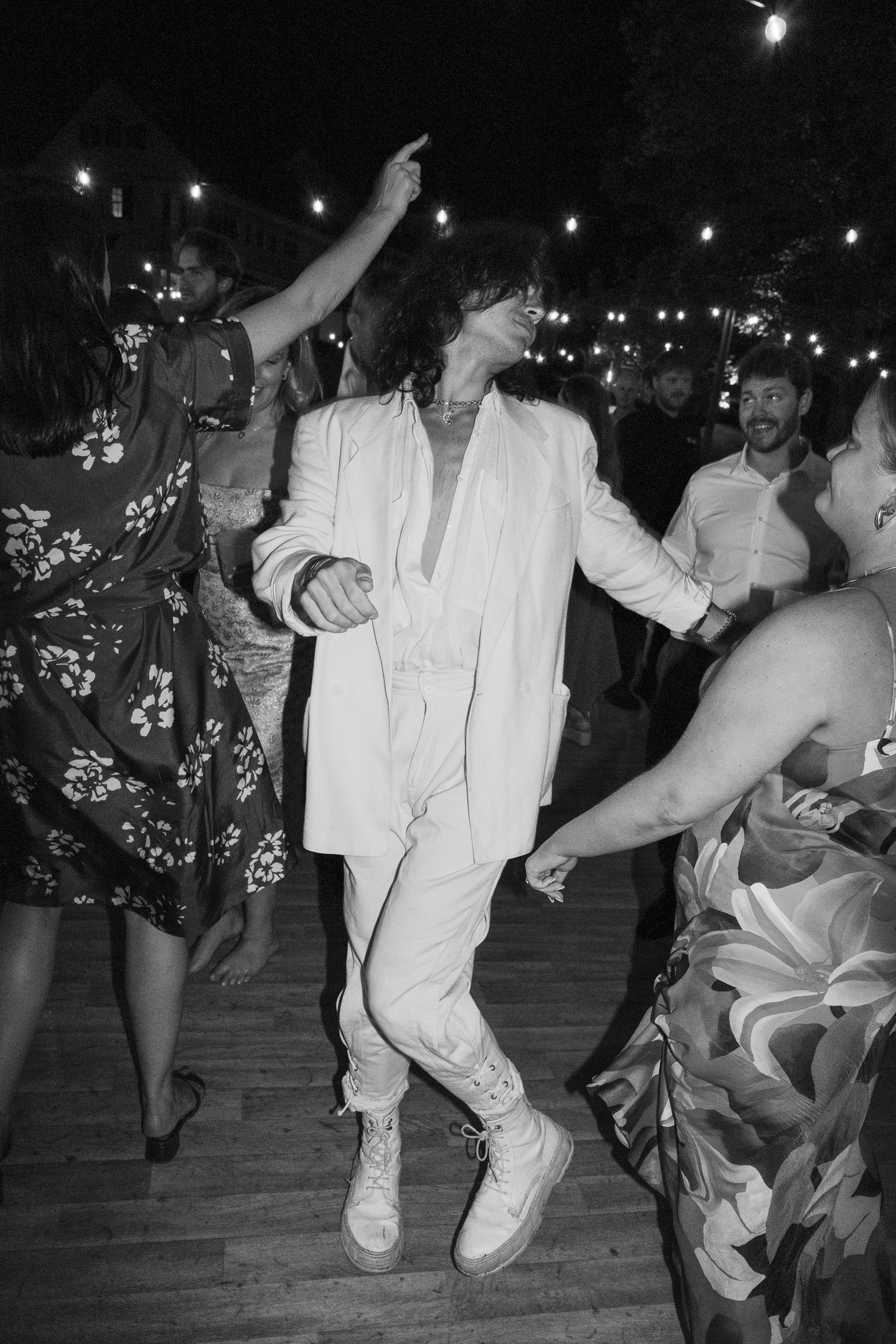 Wedding guests dancing energetically on an outdoor dance floor at night.