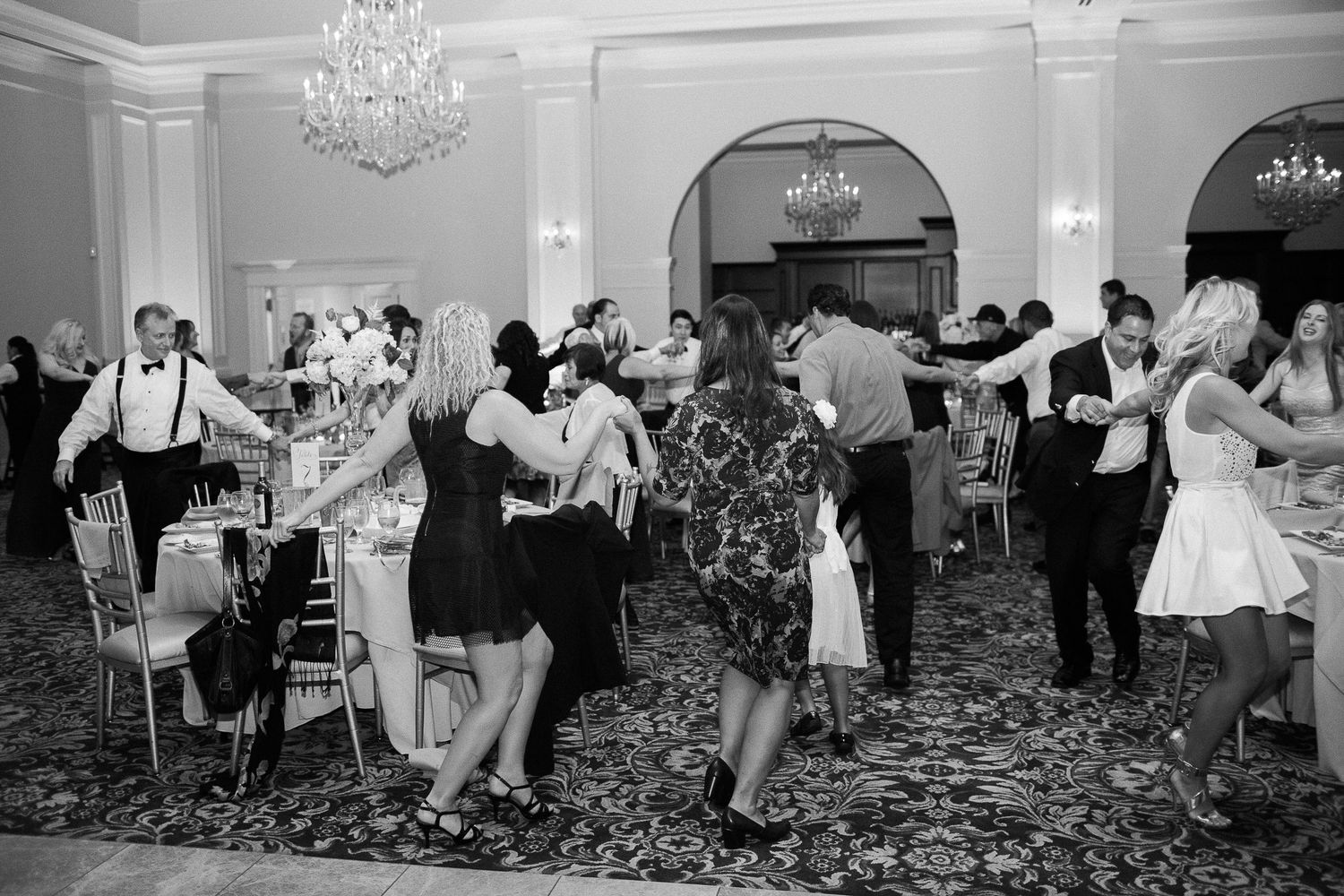 Black and white photo of wedding guests dancing and celebrating at an elegant ballroom reception.