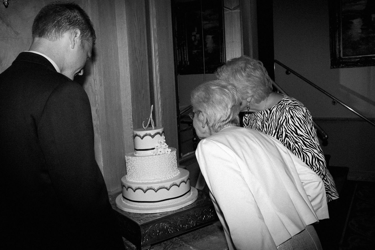 Black and white photo of two people leaning over a tiered wedding cake at a formal event.