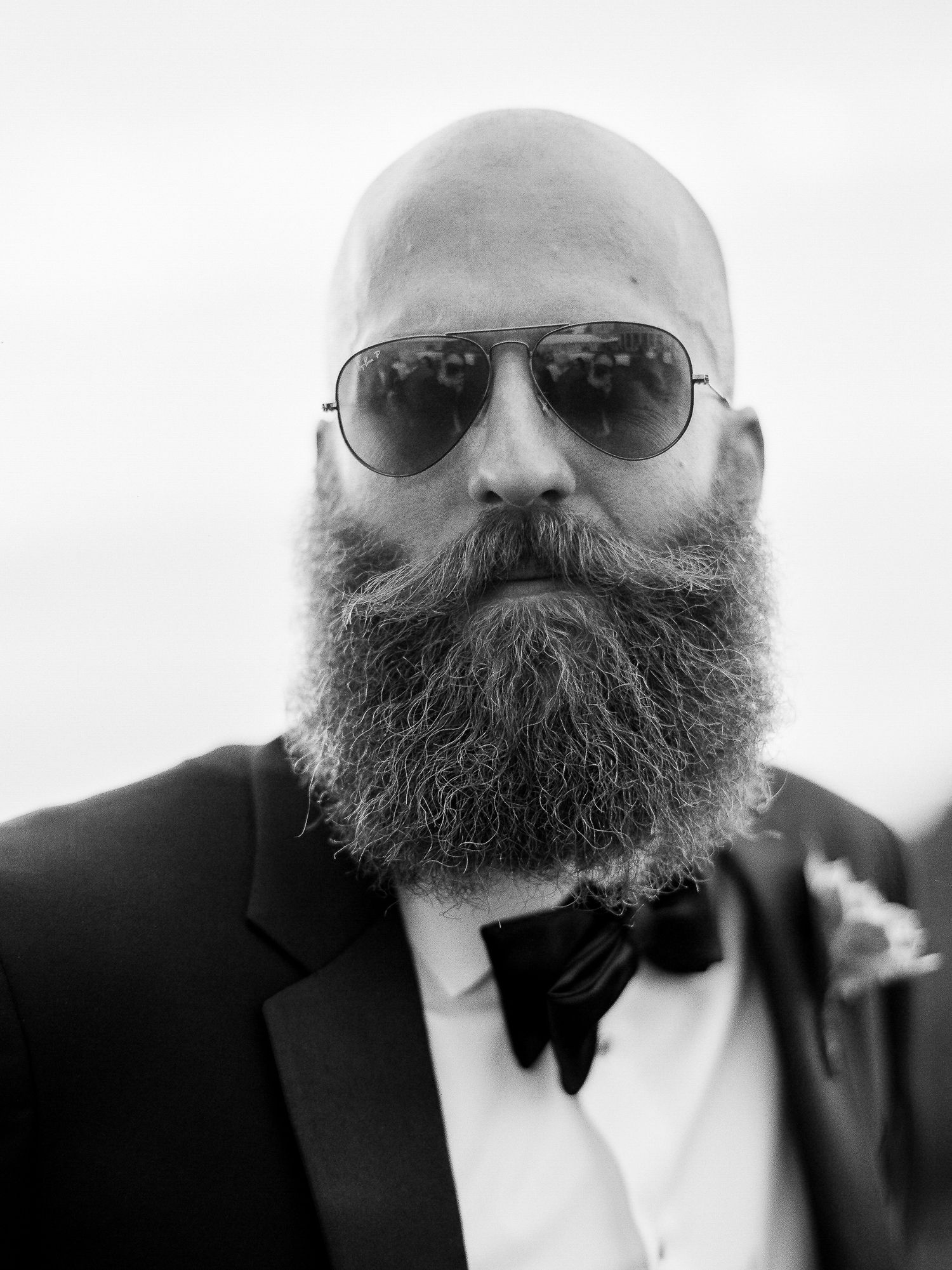 Black and white close-up portrait series showing a bald man with sunglasses and a full beard wearing a suit and bowtie.
