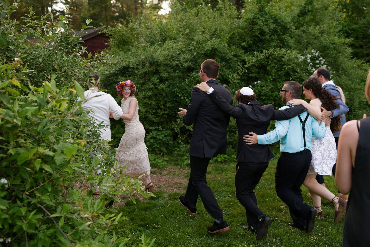 Wedding guests dance joyfully outdoors in a lush green garden during a summer celebration.