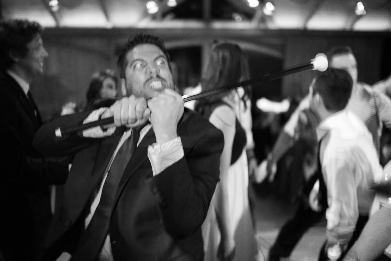 Man in suit dancing energetically at a party, holding a microphone, in black and white photography.