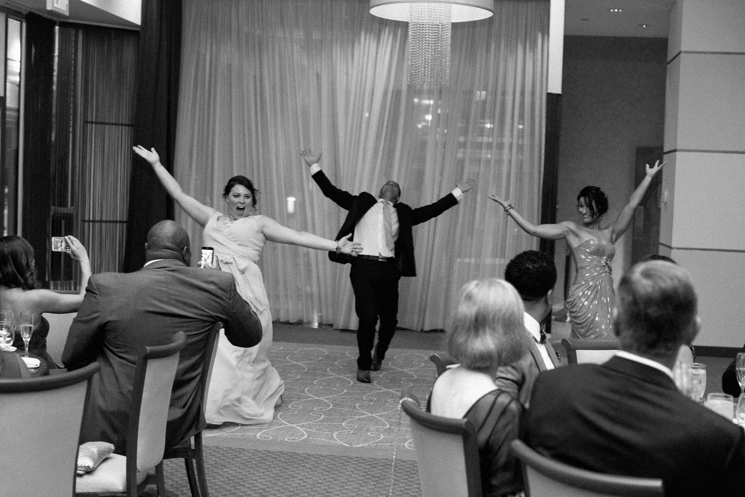 Bride, groom, and bridesmaid celebrate with raised arms during wedding reception dance performance.