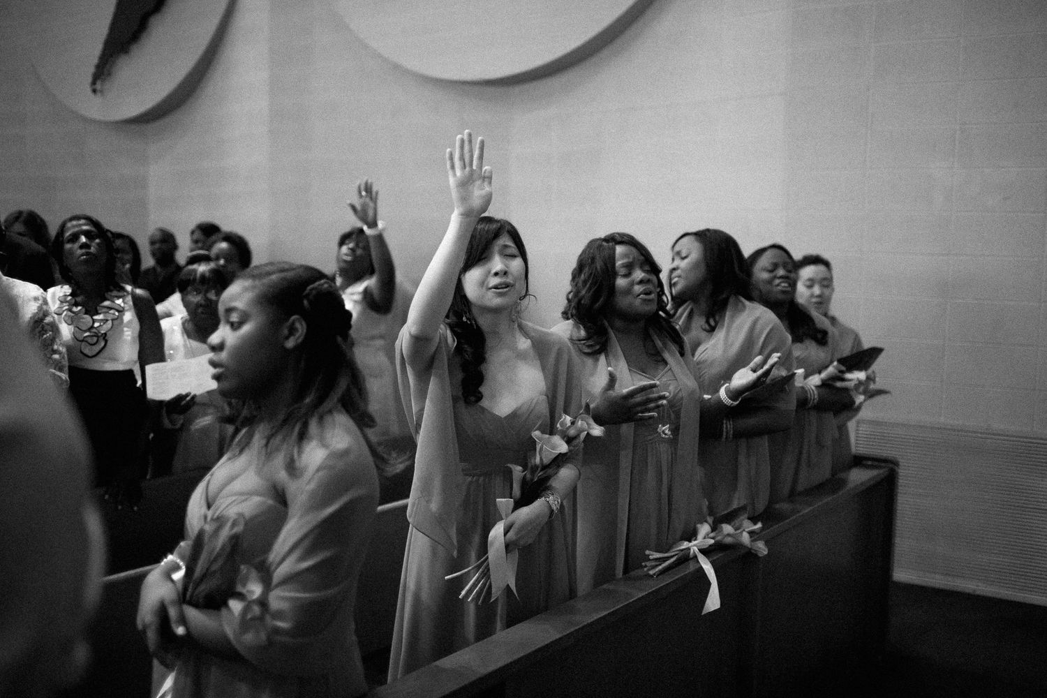 Black and white photo of diverse women worshipping in church pews, one raising her hand in praise.