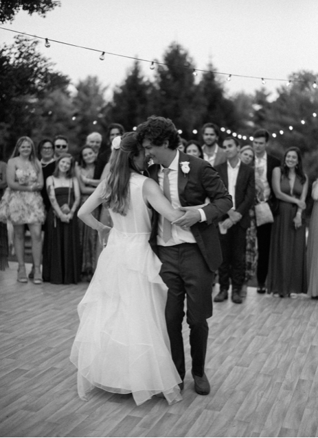 Wedding couple dancing on an outdoor patio under string lights with guests watching.
