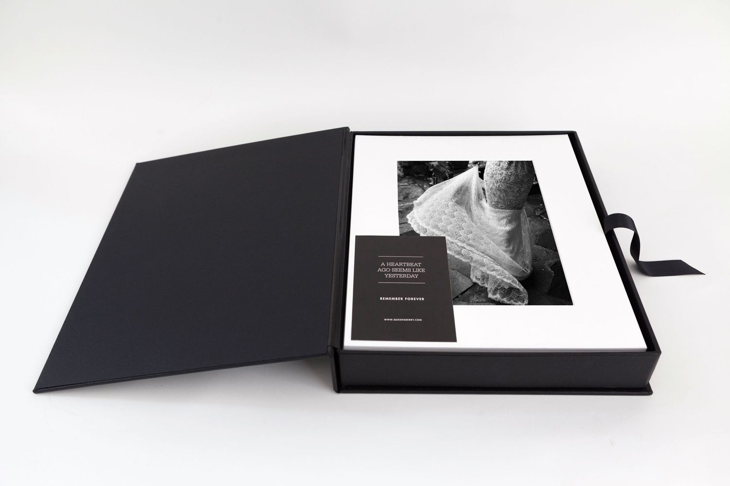 Elegant black luxury gift box open displaying a black and white fine art photograph print with a small dark card.