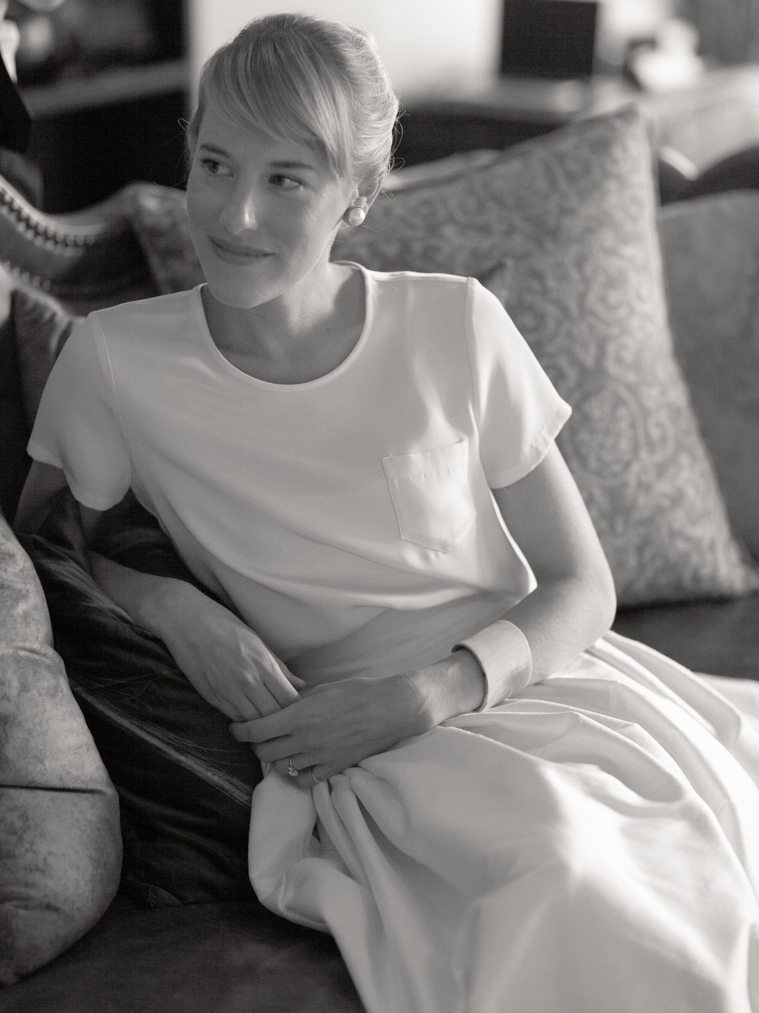 A casual portrait of someone wearing white while sitting on a couch with decorative pillows.