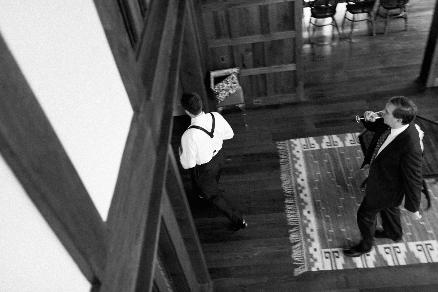 Black and white aerial view of two men in formal attire on hardwood floor with decorative rug.