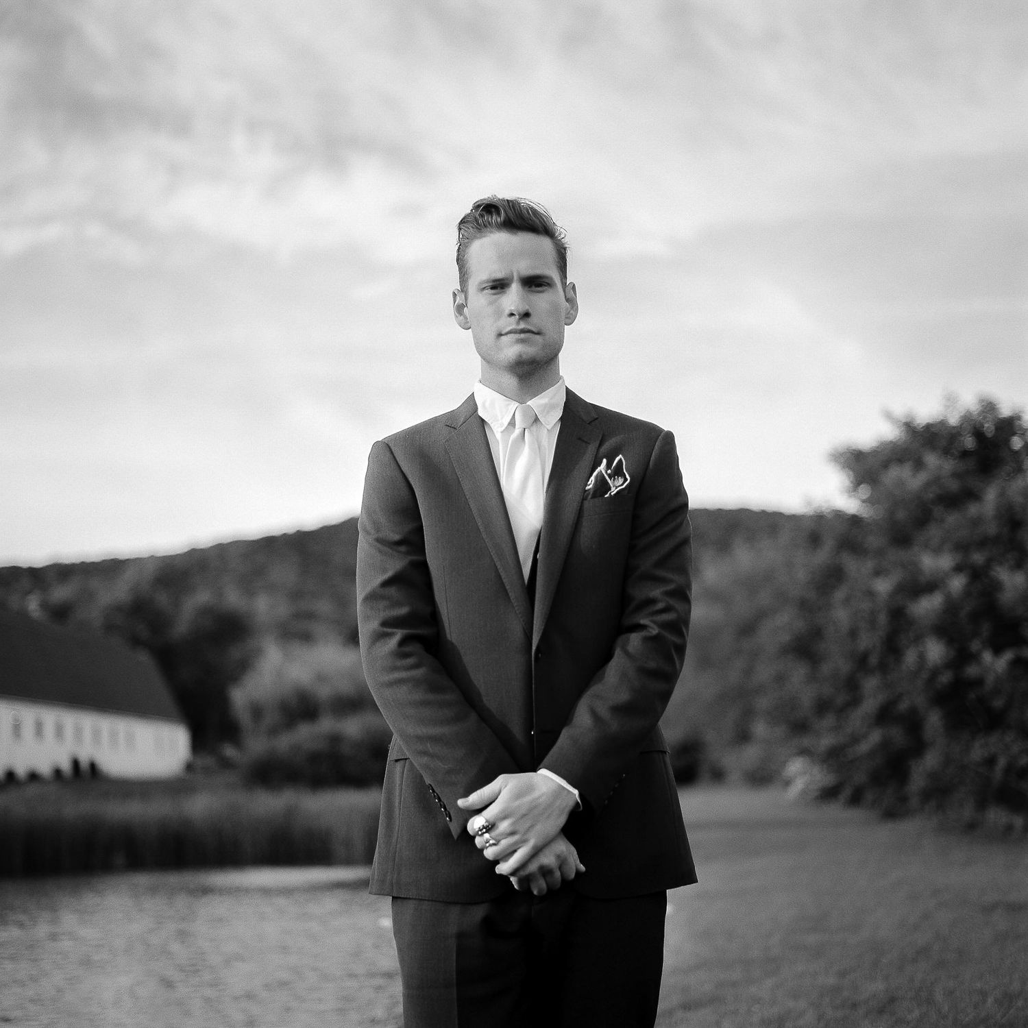 Black and white portrait of a person in formal attire standing in a scenic outdoor setting.