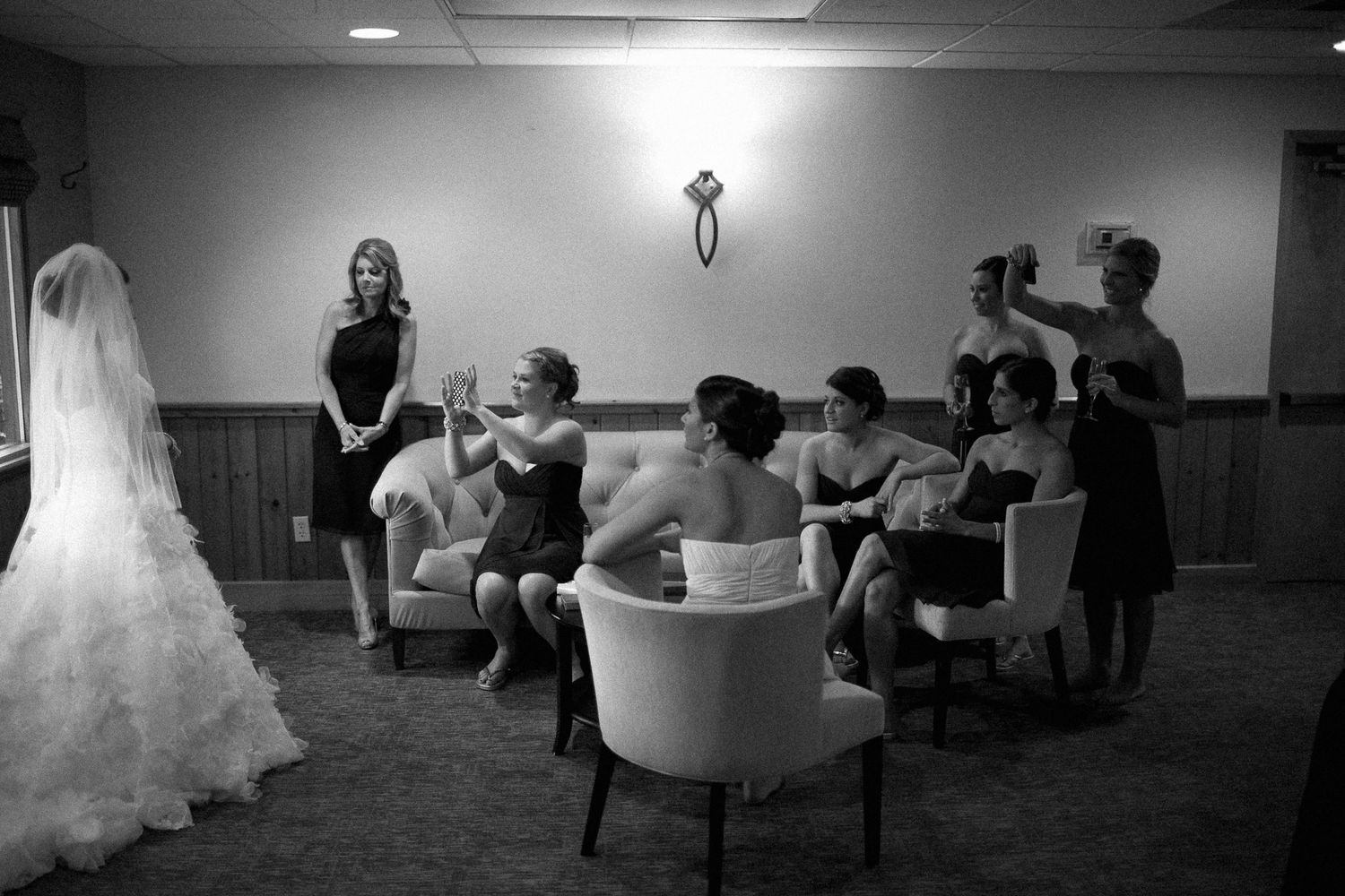 Black and white photo of bride with bridesmaids getting ready in a hotel room before the wedding ceremony.