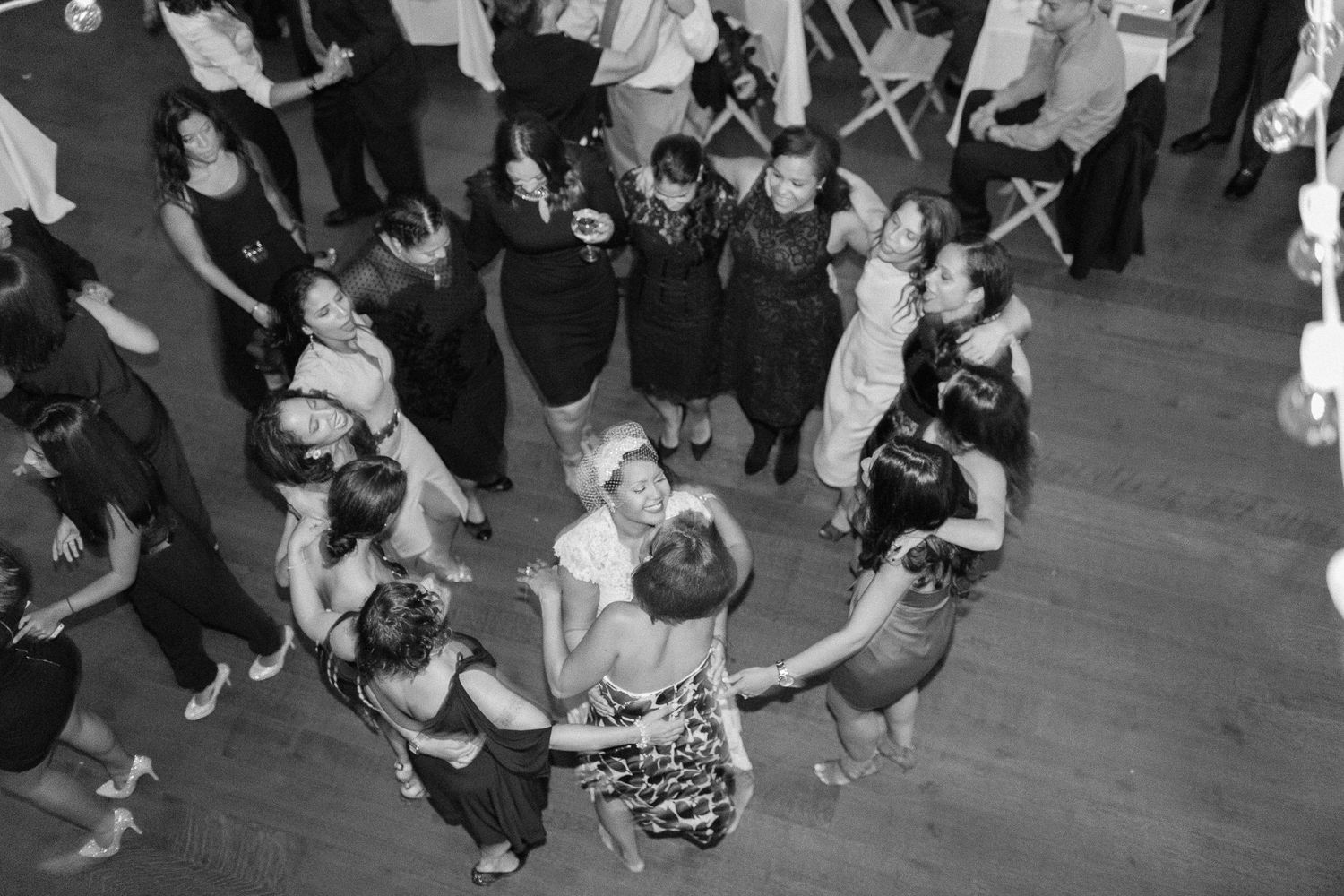 Black and white aerial view of guests dancing together on a wooden floor at a lively party or wedding reception.