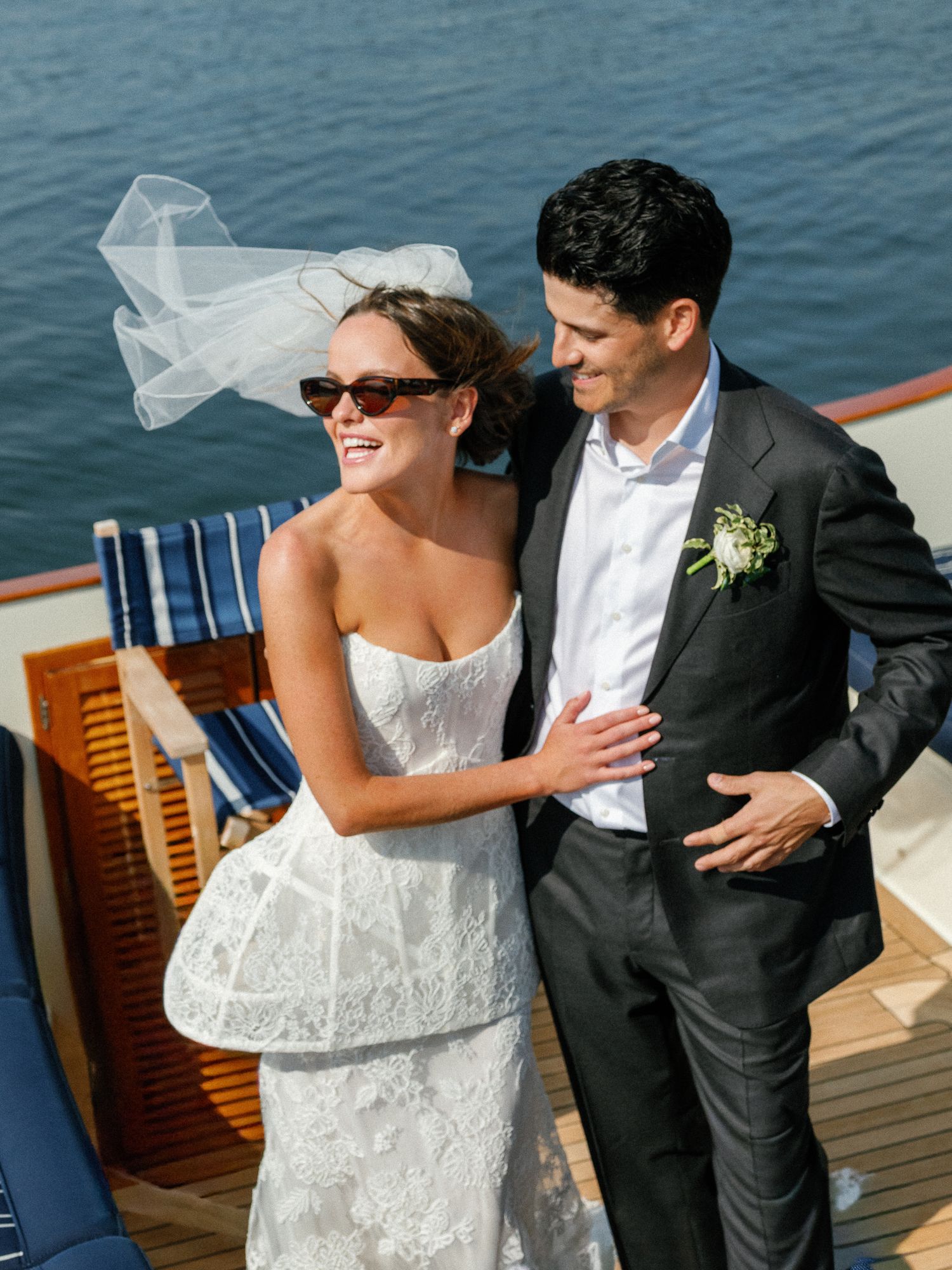 A couple in wedding attire share intimate moments on a boat deck with ocean views in the background.