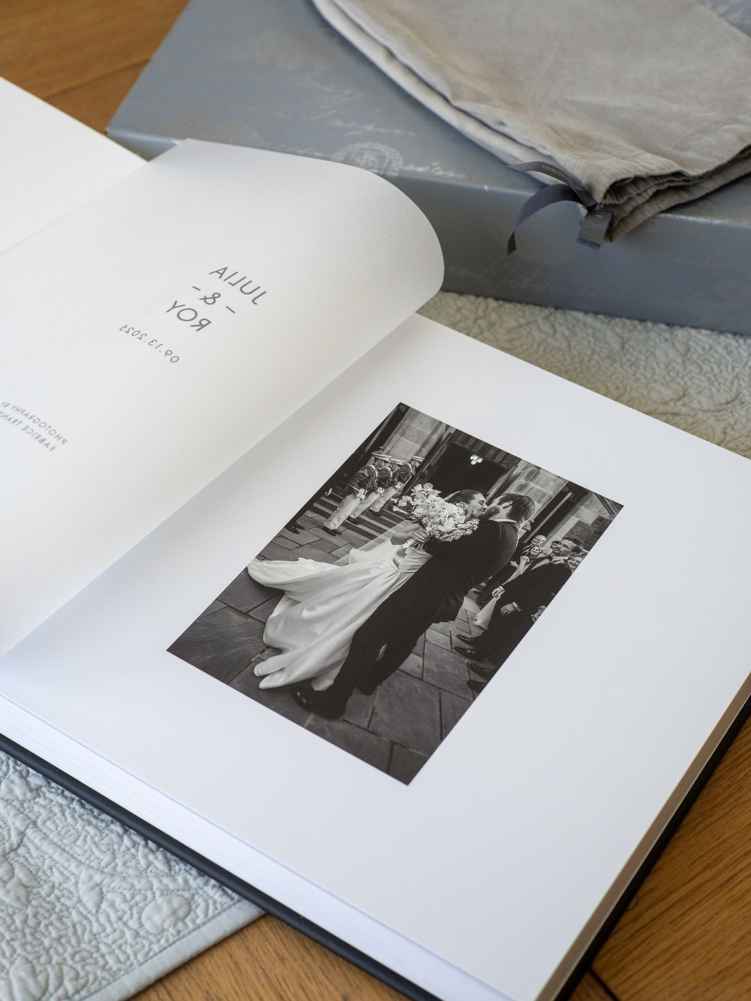An open photo book displaying black and white photographs on white pages laid out on a wooden surface.