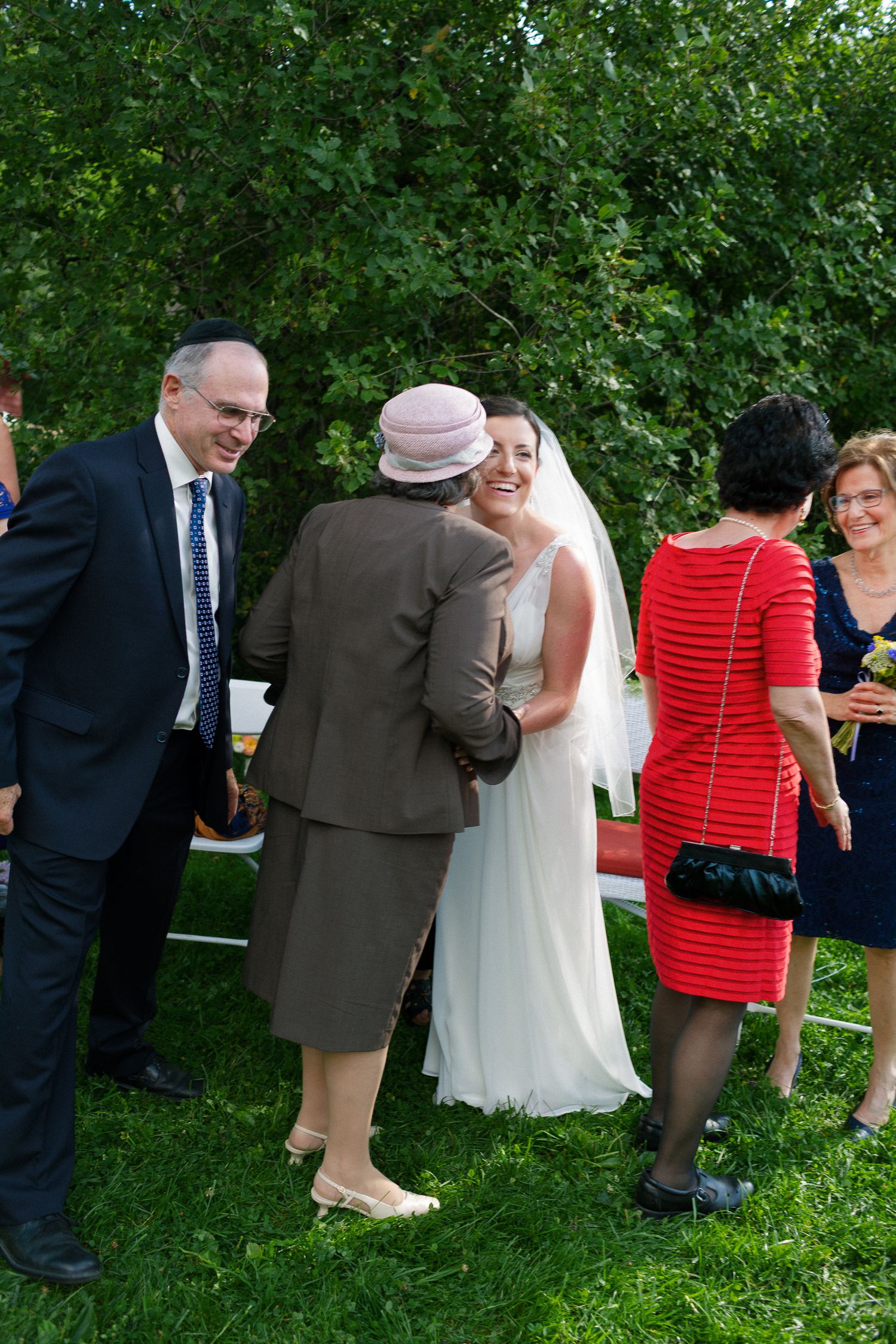 Bride in white gown smiling with elderly guest at outdoor wedding reception on green lawn.