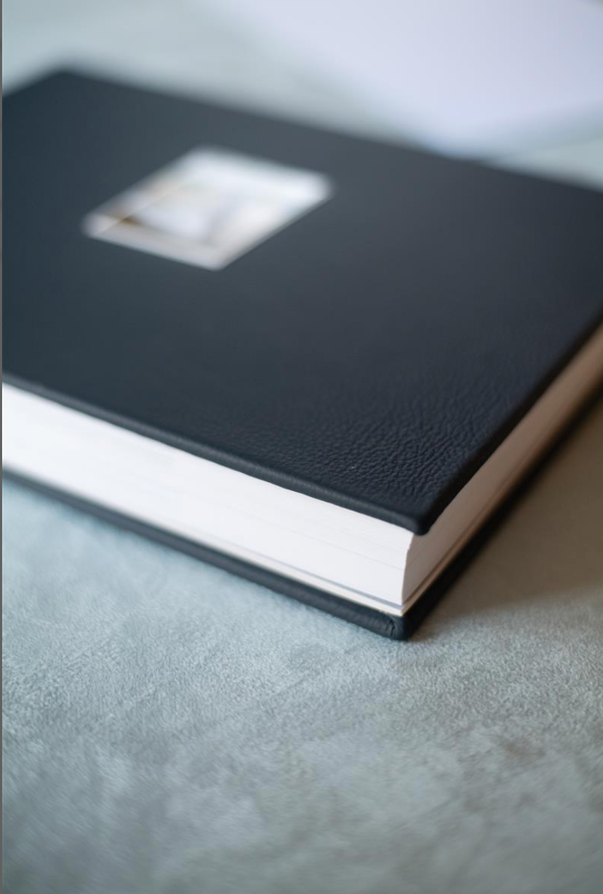 A dark navy leather-bound photo album with a small image window on the cover, resting on a gray surface.