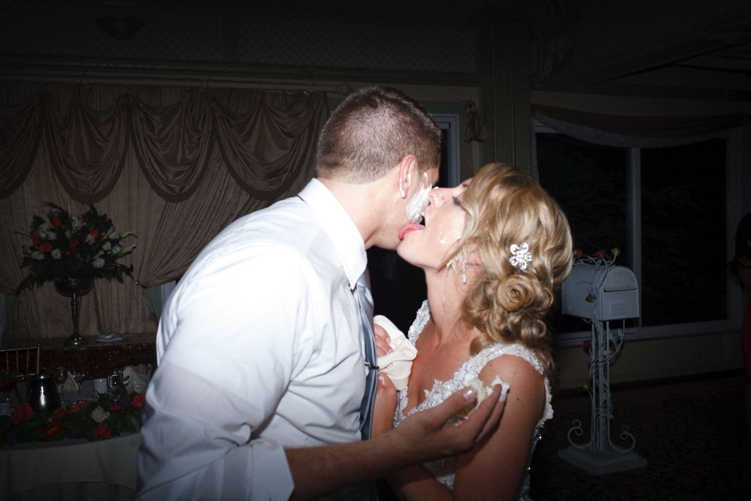 Bride and groom sharing a romantic kiss at their wedding reception in a softly lit venue.