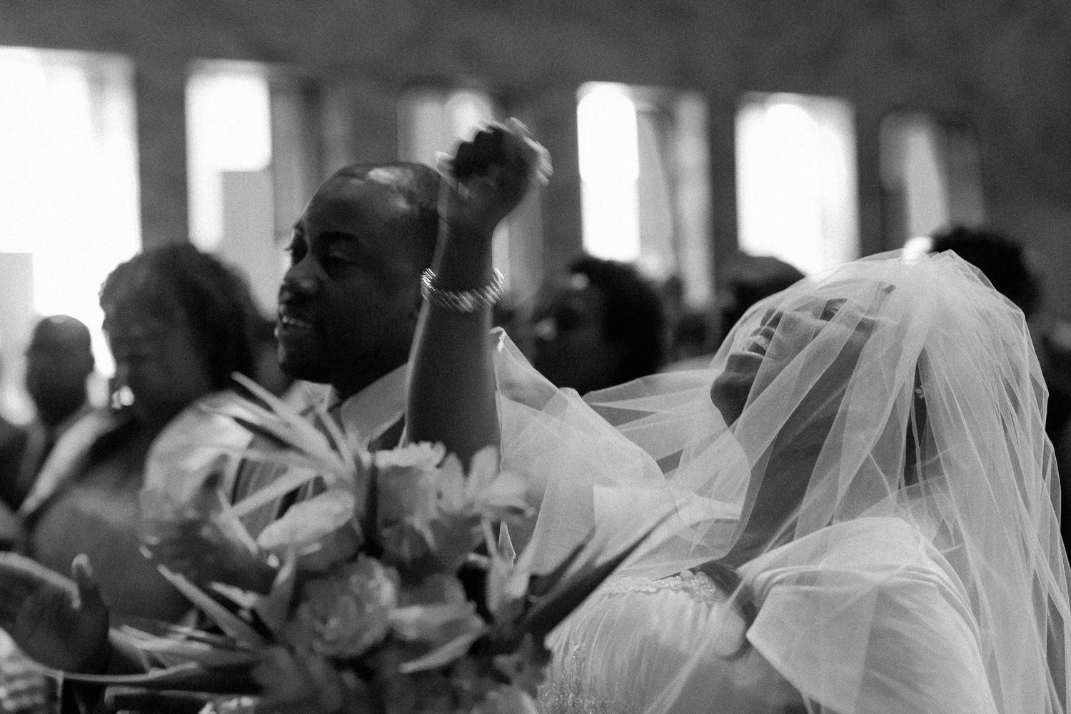 Black and white wedding photo of bride in veil and groom sharing a joyful moment during church ceremony.