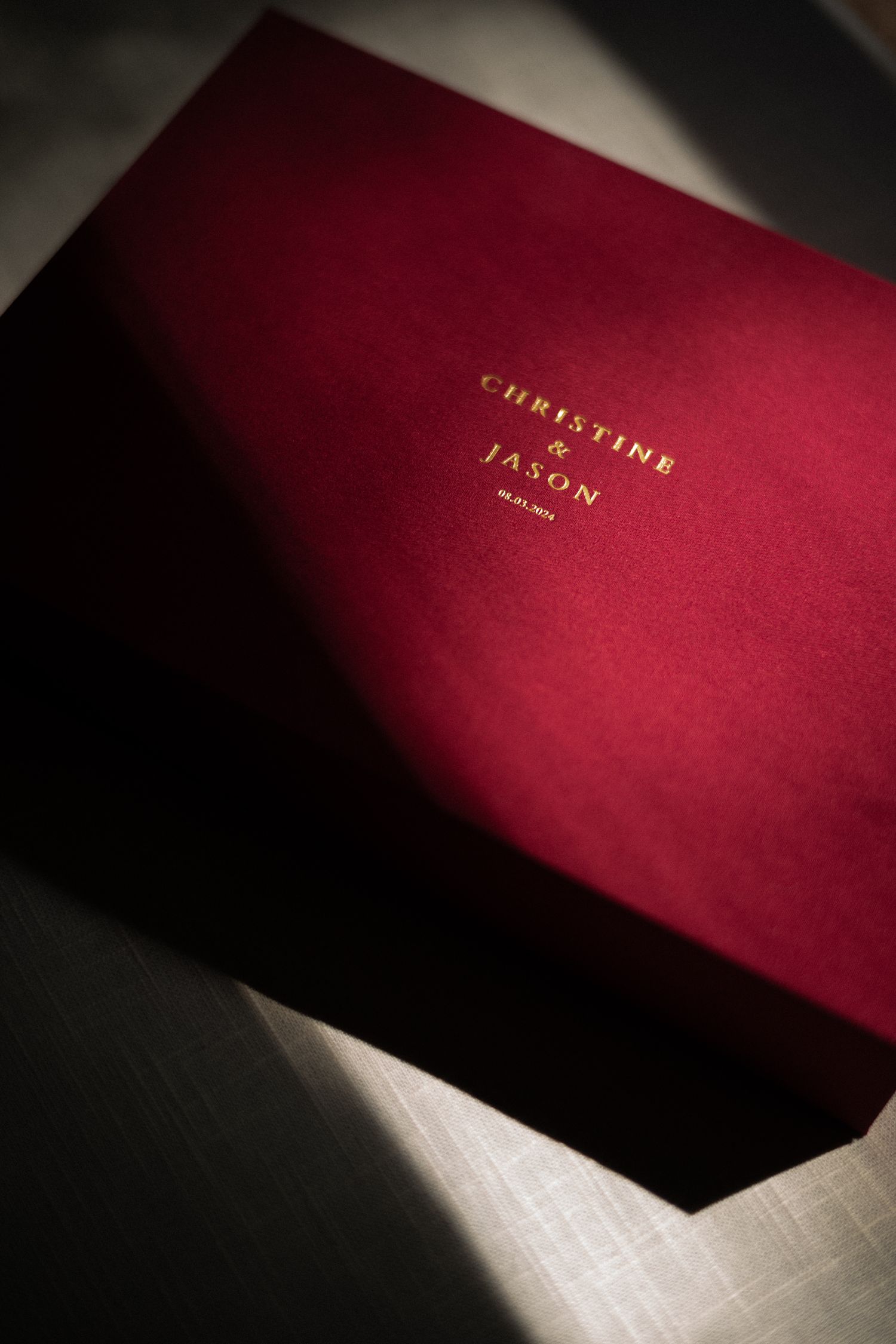 Red wedding album with gold lettering photographed in dramatic lighting.