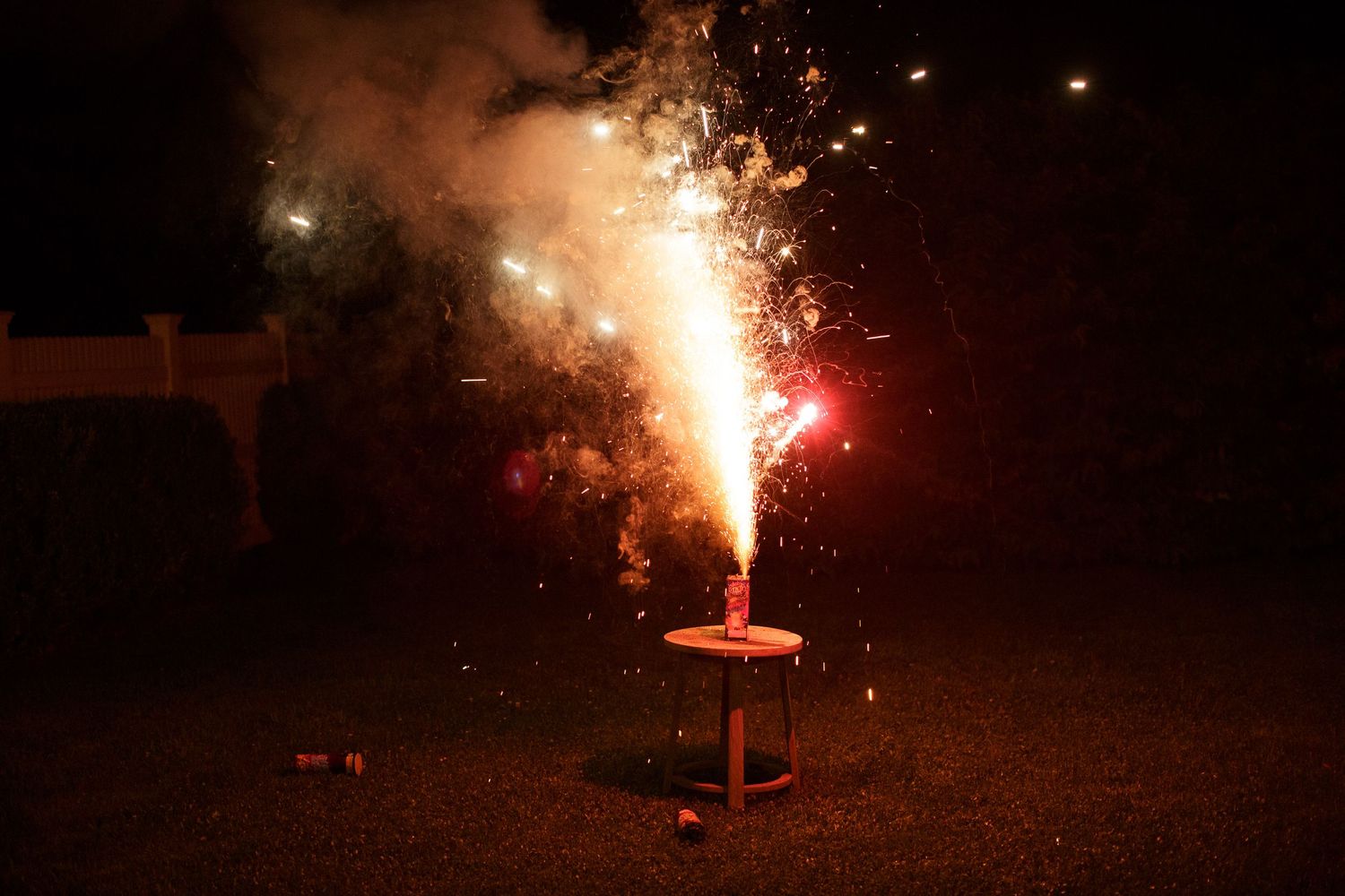 Colorful fireworks fountain sparkling on a table in a dark backyard during a nighttime celebration.