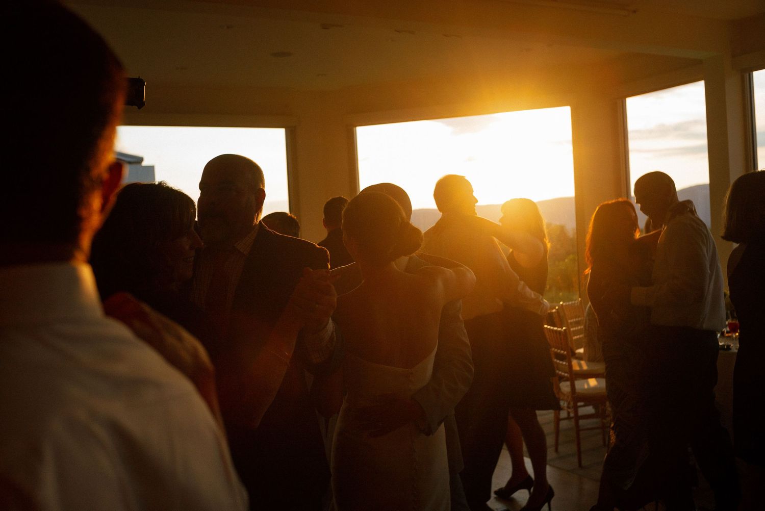Silhouettes of guests dancing at a sunset wedding reception with golden light streaming through windows.