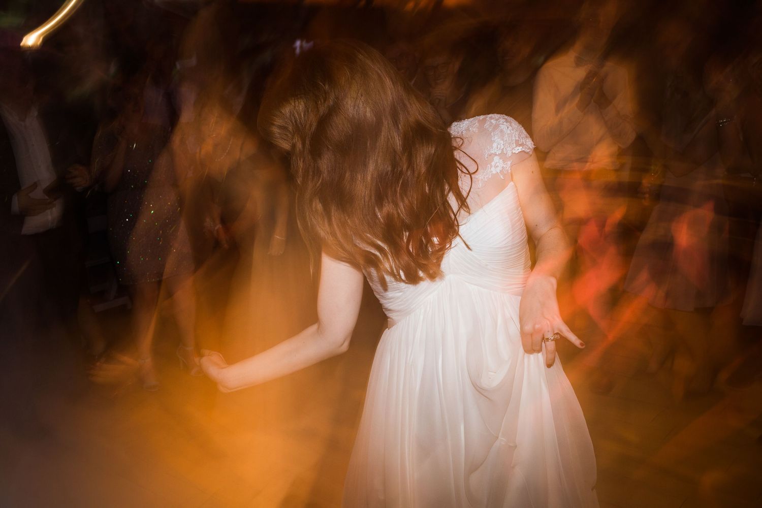 Bride in white gown dancing joyfully at wedding reception with warm golden bokeh lights swirling around her.